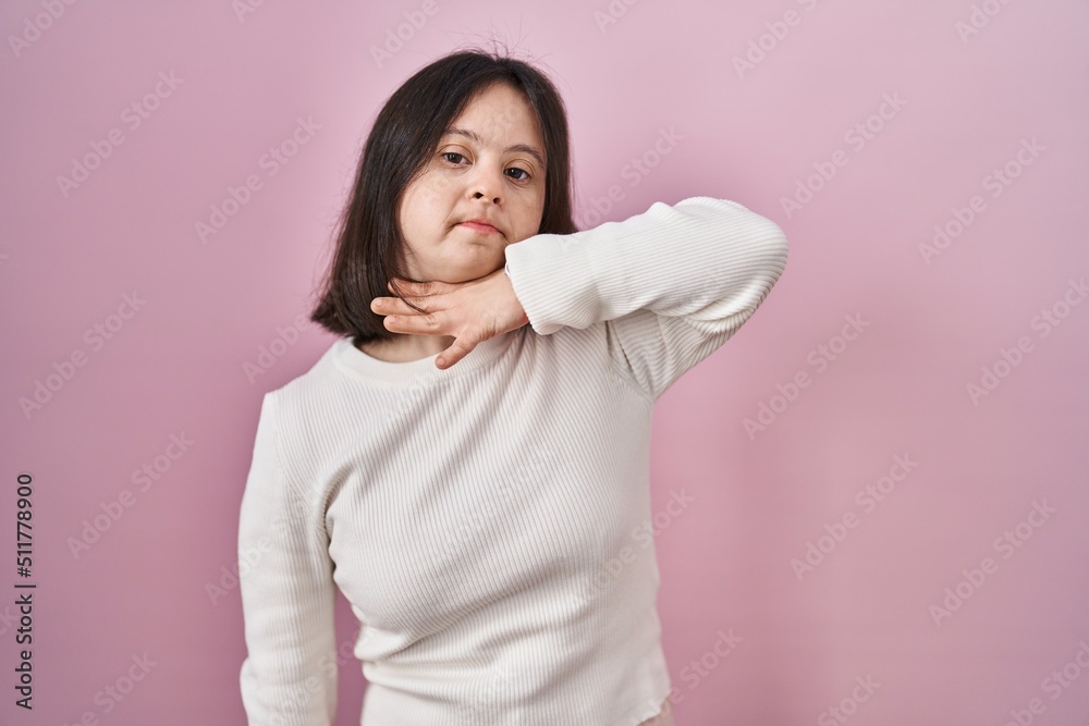 Woman with down syndrome standing over pink background cutting throat with hand as knife, threaten aggression with furious violence Woman with down syndrome standing over pink background cutting throat with hand as knife, threaten aggression with furious violence