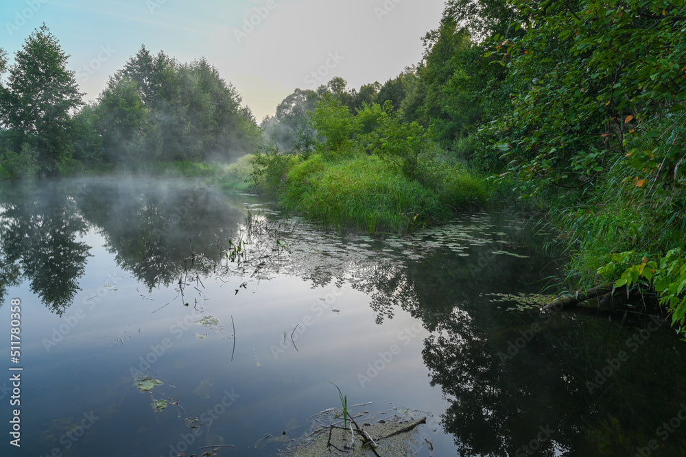 The river is covered with morning fog at sunrise, surrounded by a dense green forest. Wild nature. Active weekend vacations wild nature outdoor.