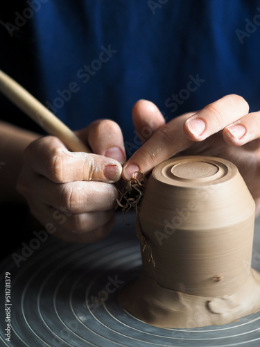 Ceramist at work using tools for creating handmade vase in studio, selective focus. Close up of female potter hands sharing handcraft crockery in studio. Small business, art, hobby concept.