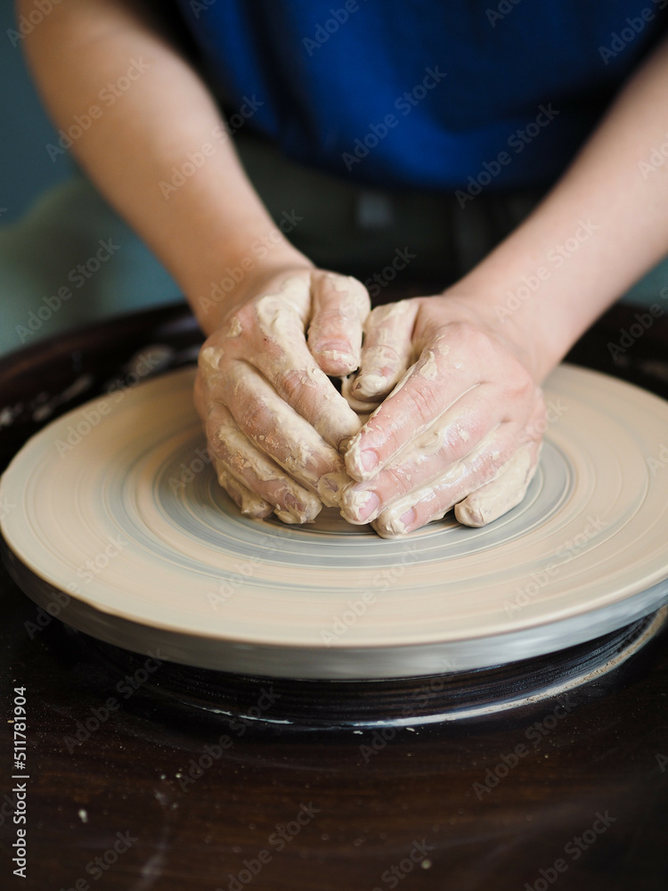Young female master working on a potter’s wheel, creates clay dishes. Ceramist young woman making clay product on pottery lathe in studio, workshop, front view. Small business, hobby, ceramic concept.
