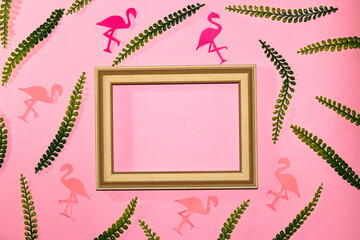 
pink background with wooden frame as copy space, around the frame flamingos of paper and jungle leaves, creative summer design