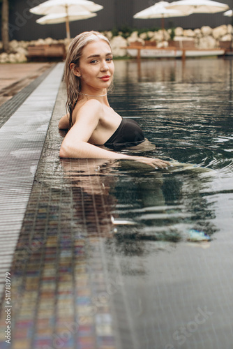 The beautiful and stylish blond woman relaxing in the pool with a cocktail in summer