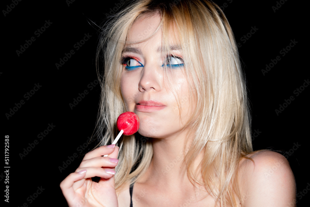 Portrait of sexy woman. Sensual blonde woman portrait with bright make up looking forward, licking red candy lollipop, studio black background. Portrait of sexy woman. Sensual blonde woman portrait with bright make up looking forward, licking red candy lollipop, studio black background.