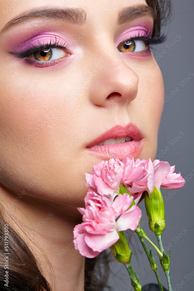 Closeup portrait of female face with pink beauty makeup and carnation flowers near lips. Closeup portrait of female face with pink beauty makeup and carnation flowers near lips.