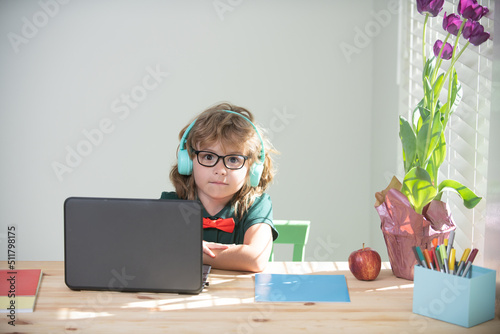 Child boy in room at home school. Education, elementary school, learning and people concept. Kid with headphones have video call using laptop, study online on computer, homeschooling.