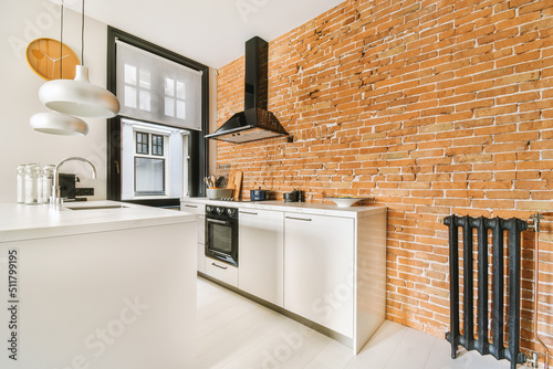 Open plan kitchen design with stone countertops, hanging lamps, brick wall , wide black framed window and radiator