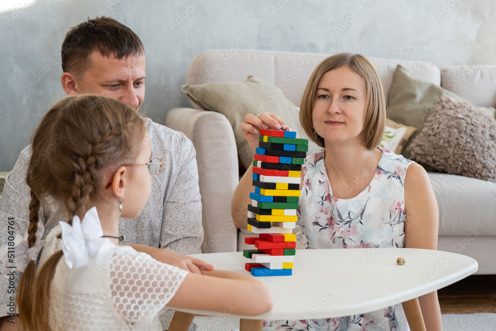 Family of Three Playing Jenga Board Game with Wooden Bars while Sitting around a Table at Home