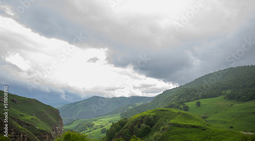 Beautiful spring landscape in the Caucasus Mountains with lush grassy hills and rocky slopes. Dramatic cloudy sky on a rainy day. Low clouds on the tops of the mountains.