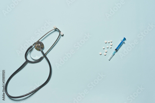 A disposable syringe for injection, stethoscopen and white round tablets on a blue background. photo