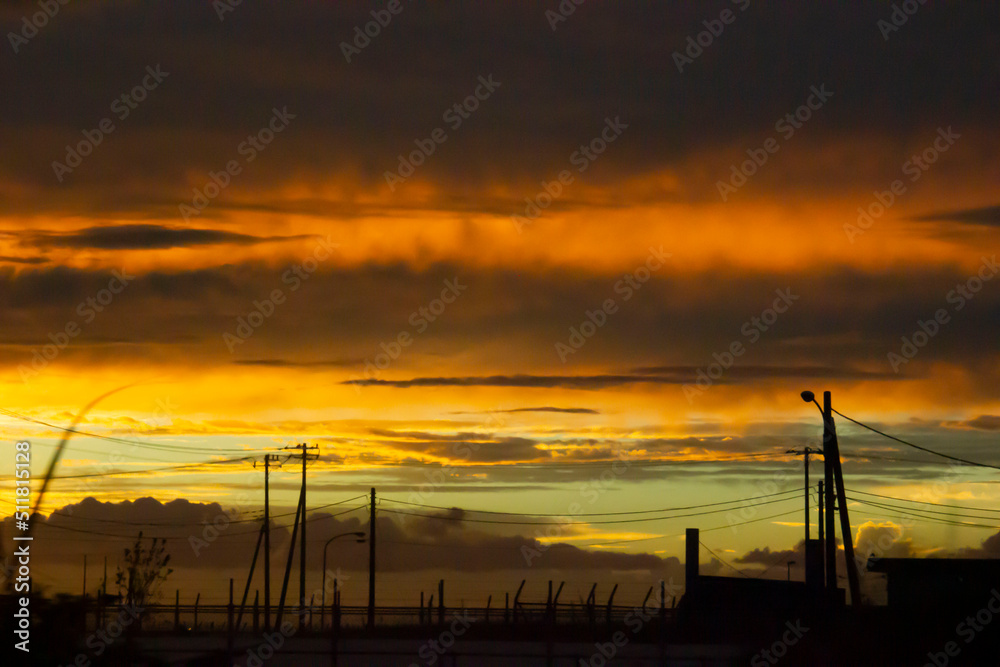 水色とオレンジ色の夕焼けに浮かぶ野原の電柱群のシルエット