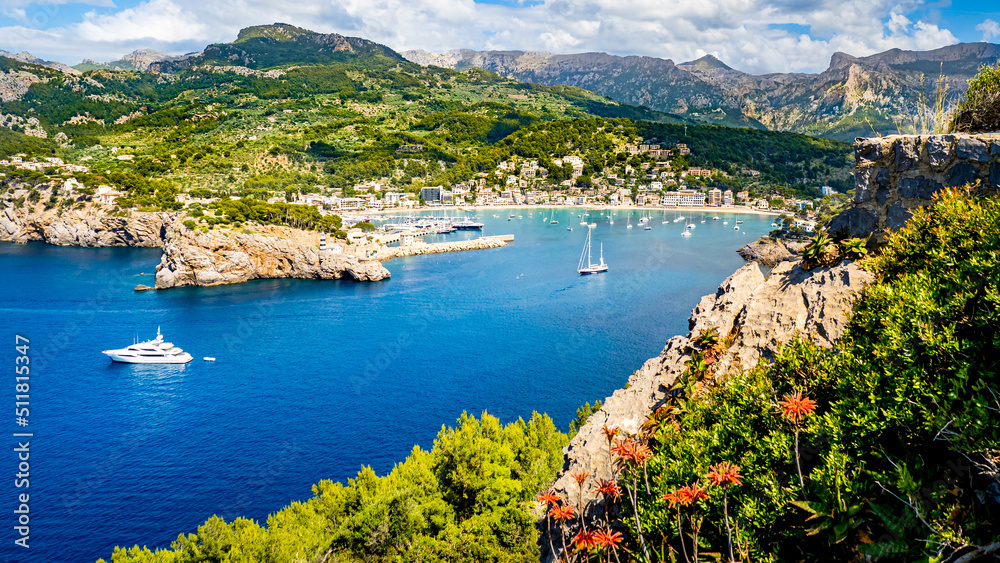 Panorama of the harbor entrance of marina Tramontana in Port de Soller Mallorca in summer with mountains of Serra de Tramuntana in the background, Sóller beaches, boats and flowers in the foreground.