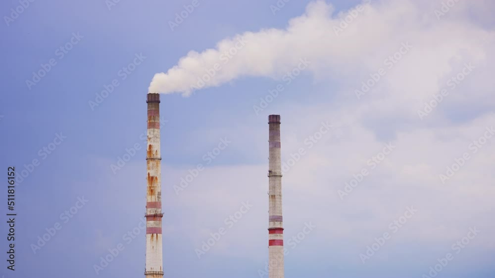 Old high pipes from industrial plant. Rusty pipes, one of which producing smoke into atmosphere. Blue sky backdrop. Old high pipes from industrial plant. Rusty pipes, one of which producing smoke into atmosphere. Blue sky backdrop.