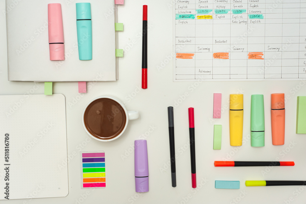 Colorful stationery, a school schedule and a cup of cocoa are laid out on a white table. Colorful stationery, a school schedule and a cup of cocoa are laid out on a white table.