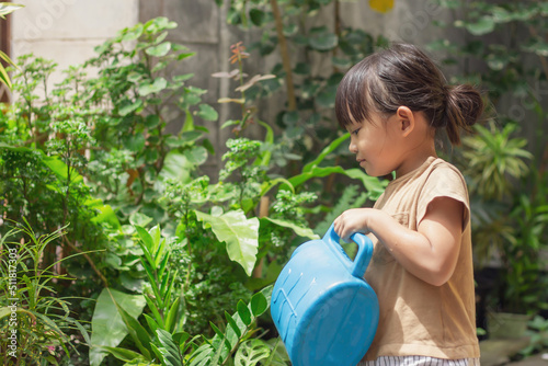 Portrait  image of 4-5 years old kid girl. Happy Asian child girl watering the green tree by water can at her backyard. Gardening in summer or spring season. Activity of children. Learning concept.