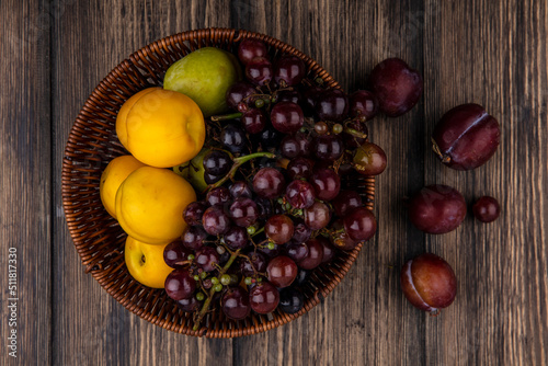 top view of fruits as grape pluot nectacots in basket and flavor king pluots on wooden background photo