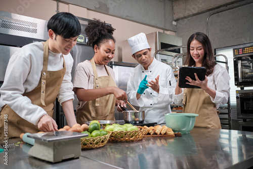 Hobby cuisine course, senior male chef in cook uniform teaches young cooking class students to prepare, mix and stir ingredients for pastry foods, fruit pies in restaurant stainless steel kitchen.