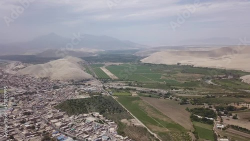 Panning aerial view of drone of a city of buildings and houses and farm fields next to it with rivers and hills and desert and dunes on the day with a clear sky in 4k at  Casma, lima, peru photo