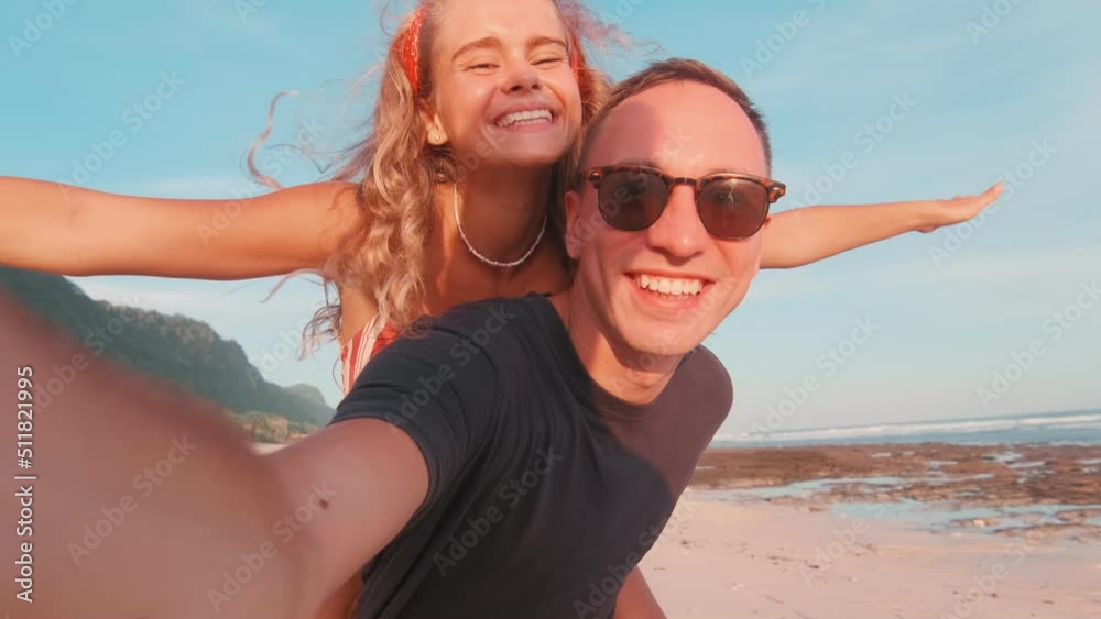 Young happy Caucasian couple man and woman have good time together at sea resort record videos twirling on sand enjoy holiday together on beach next to ocean. Summer travel, lifestyle, love Young happy Caucasian couple man and woman have good time together at sea resort record videos twirling on sand enjoy holiday together on beach next to ocean. Summer travel, lifestyle, love