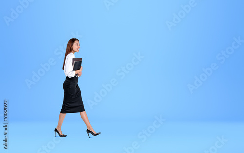 Young businesswoman with notebook, walking on blue background. C