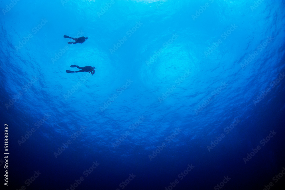 Blue ocean background with a lot of copy space and a silhouette of a couple of divers