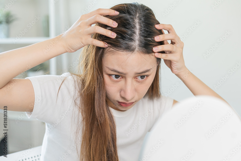 Naklejka premium Damaged Hair, face serious asian young woman worry looking at scalp in mirror, hand in break into front hair loss, thin problem symptom at home. Health care shampoo beauty, isolated on background.