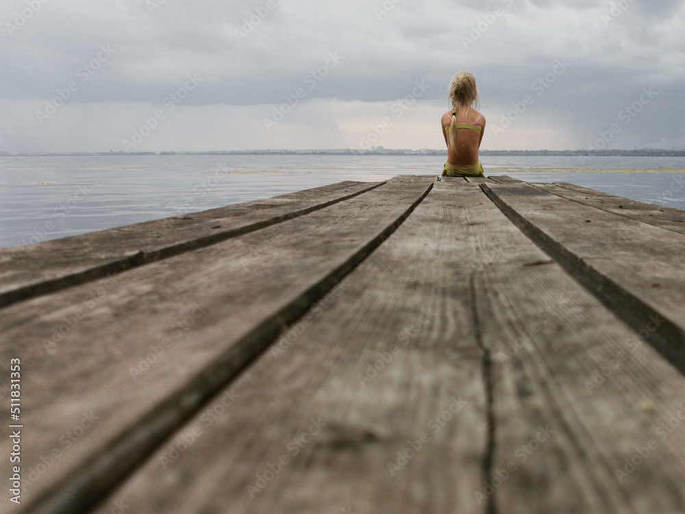 the concept of loneliness, sadness. a small child sits alone on a bridge the concept of loneliness, sadness. a small child sits alone on a bridge