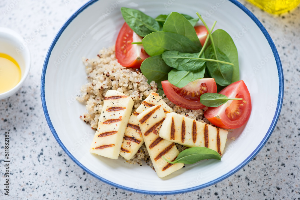 Quinoa with grilled halloumi cheese, fresh spinach and red tomatoes served in a white plate, middle close-up, studio shot Quinoa with grilled halloumi cheese, fresh spinach and red tomatoes served in a white plate, middle close-up, studio shot