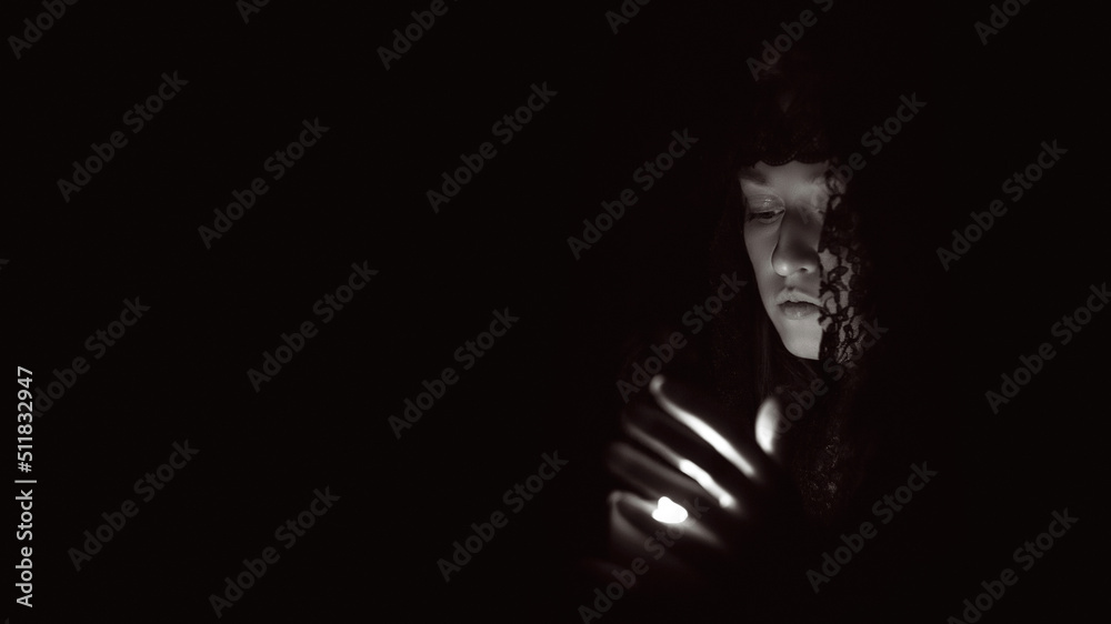 Woman in a black hood with a lit candle in her hands, black and white photo Woman in a black hood with a lit candle in her hands, black and white photo