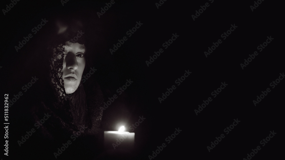 Woman in a black hood with a lit candle in her hands, black and white photo Woman in a black hood with a lit candle in her hands, black and white photo