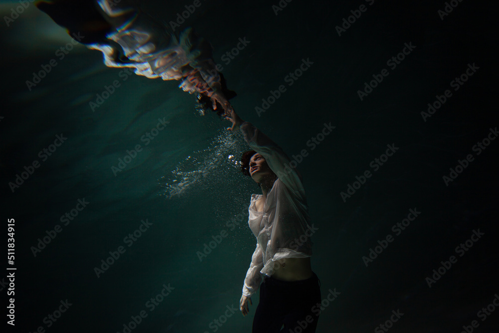 underwater shooting with contrasting light, a guy is swimming underwater, pulling his hand to his reflection in the surface of the water. Subconsciousness and self-reflection, concept underwater shooting with contrasting light, a guy is swimming underwater, pulling his hand to his reflection in the surface of the water. Subconsciousness and self-reflection, concept