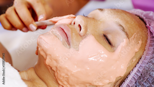 Cosmetologist applies a scrub on female face. Woman in a spa salon on cosmetic procedures for facial care.