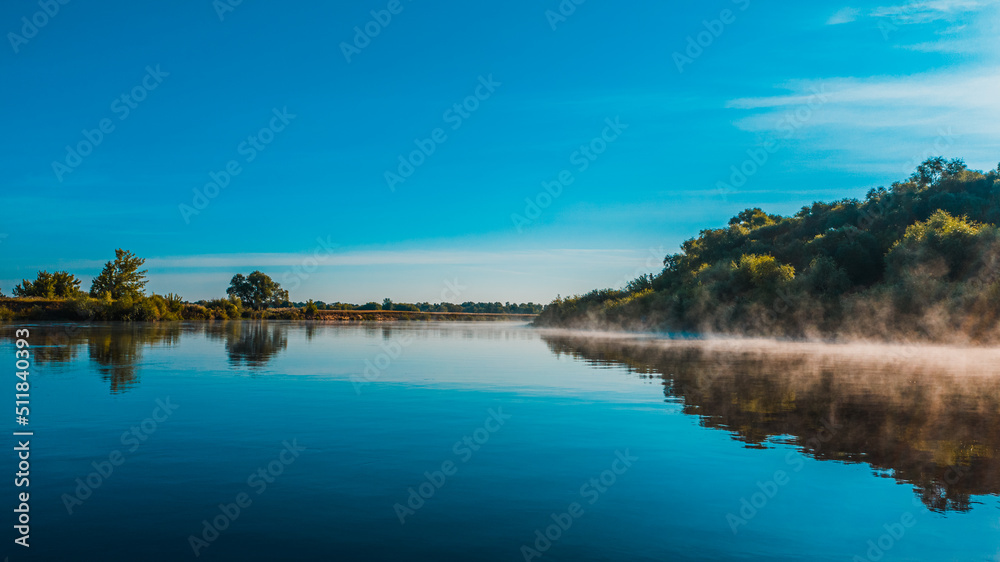 Aerial  view of a beautiful summer  landscape over river while dawn. Top view over river with a smooth water surface reflecting blue sky. Morning evaporation on a river while sunrise.