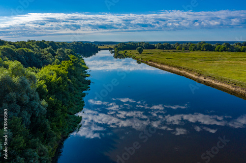 Aerial view of a beautiful summer landscape over river while dawn. Top view over river with a smooth water surface reflecting blue sky and clouds.