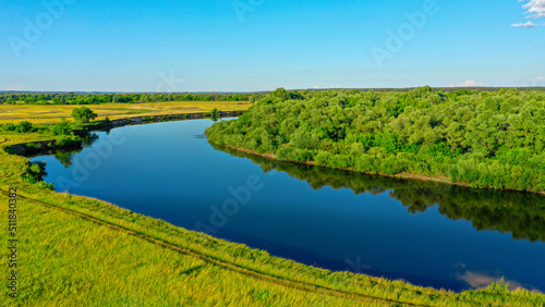 Aerial view of a beautiful summer landscape over river while dawn. Top view over river with a smooth water surface reflecting blue sky.