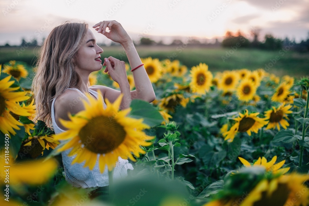 A young, slender girl with loose hair in a T-shirt stands in a field of sunflowers at sunset A young, slender girl with loose hair in a T-shirt stands in a field of sunflowers at sunset