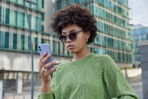 Fotografia Photo of stylish curly haired young woman wears sunglasses and green jumper chec