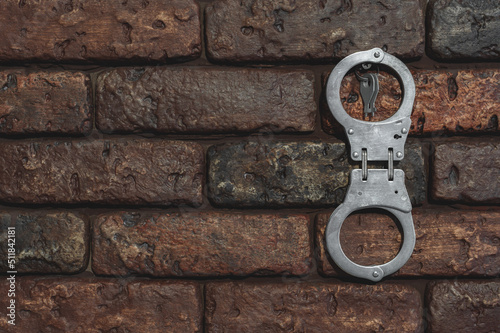Handcuffs with keys are hanging on a brick wall.