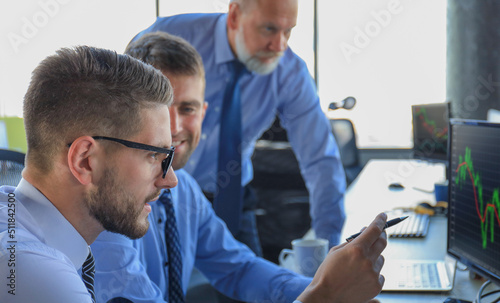 Group of modern business men in formalwear analyzing stock market data while working in the office.