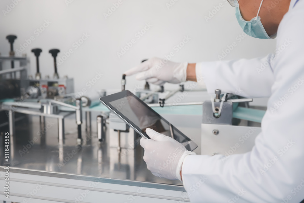 Doctor engineer or scientist in face mask using computer tablet working with medical mask production machine factory Doctor engineer or scientist in face mask using computer tablet working with medical mask production machine factory