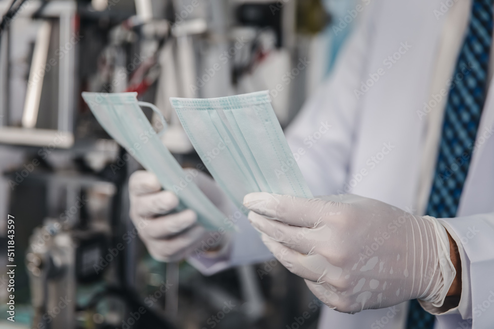Doctor hand in glove holding checking face mask at a production machine manufacturing factory