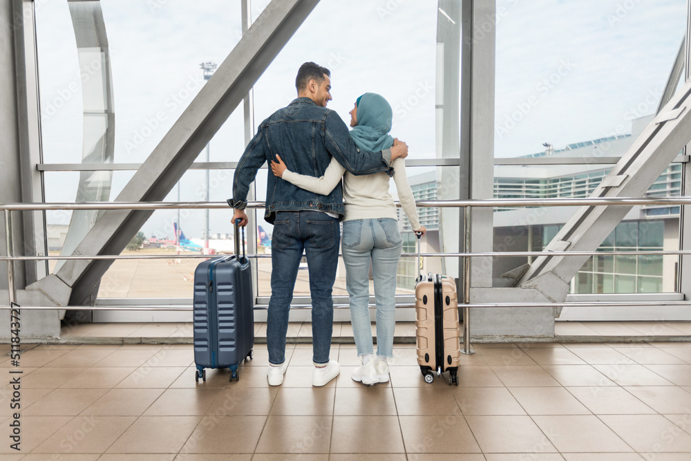 Romantic Travel. Loving Muslim Couple Standing With Suitcases Near Window In Airport Romantic Travel. Loving Muslim Couple Standing With Suitcases Near Window In Airport