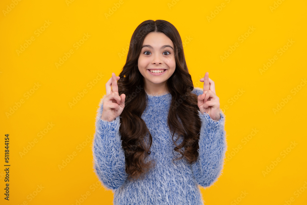 Happy teenager, positive and smiling emotions of teen girl. Teenager child holding fingers crossed for good luck. Girl prays and hopes dreams come true, isolated on yellow background.