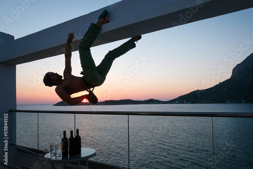 Can’t stop climbing. Climber (man) hanging on the balcony above wine bottles at sunset Kalymnos island, Greece.