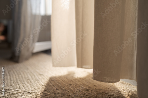 Closeup photo of jute rug on a floor with curtains on background with warm sun light
