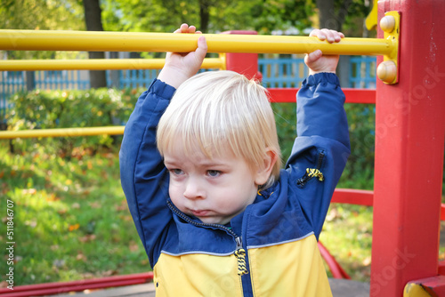 Portrait of two years old child boy at colourful playground area. Autumn public park. Little blond boy playing outdoors. Happy kid on a jungle gym. Sport and lifestyle Concept
