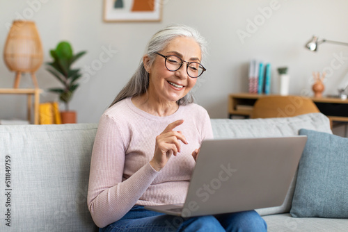 Happy senior european gray-haired female in glasses have video call by laptop, chatting in social networks