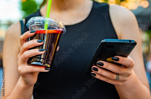 Obraz na plátně woman hand holding phone and plastic cup with sangria drink on street