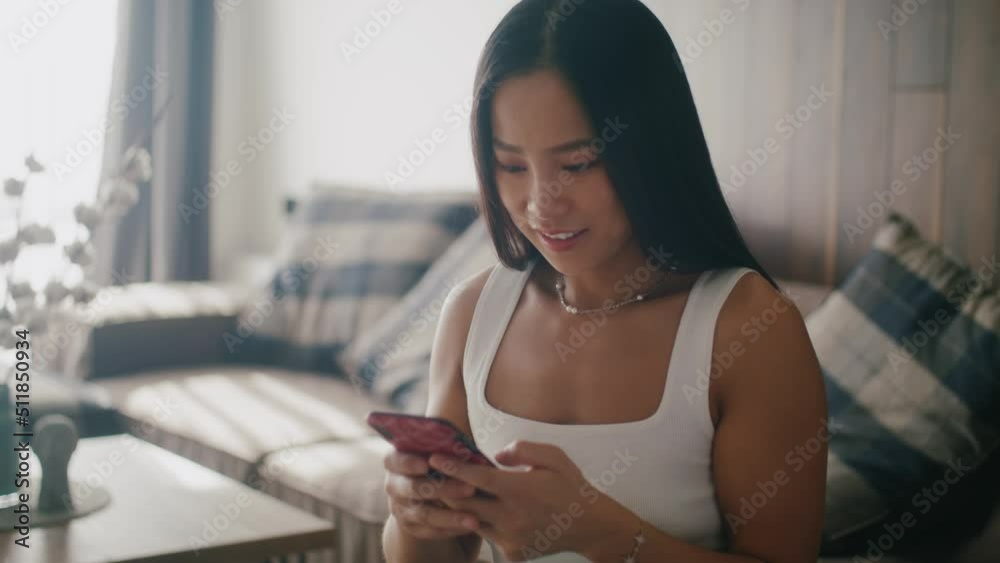 Close up young asian woman holding smart phone laughing enjoying using mobile sitting at home at sunlight. Portrait. Slow motion Close up young asian woman holding smart phone laughing enjoying using mobile sitting at home at sunlight. Portrait. Slow motion