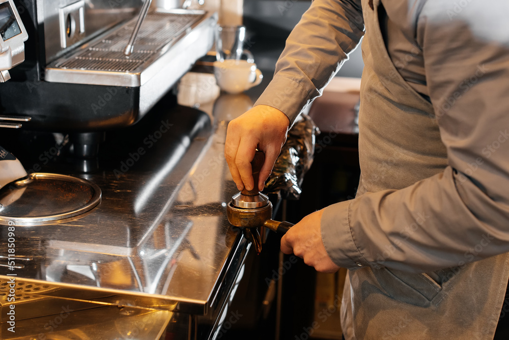 Close-up of a masked bartista preparing delicious delicious coffee at the bar in a coffee shop. The work of restaurants and cafes during the pandemic. Close-up of a masked bartista preparing delicious delicious coffee at the bar in a coffee shop. The work of restaurants and cafes during the pandemic.