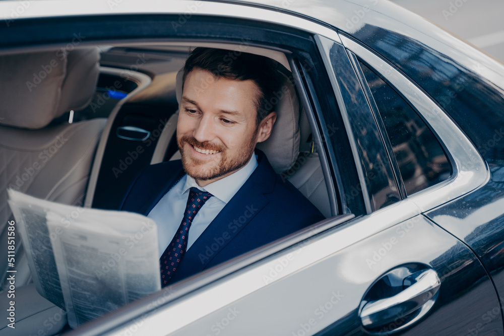 Handsome young banker in smart formal tuxedo suit reads newspaper in luxury auto Handsome young banker in smart formal tuxedo suit reads newspaper in luxury auto